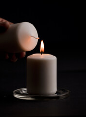 burning candle with flame, man's hands lighting candle, black background. (focus on candle)