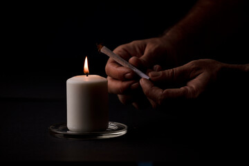 candle lit with flame, man's hands holding a cigar, black background. (focus on candle).