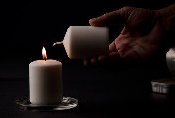 burning candle with flame, man's hands lighting candle, black background. (focus on candle)