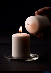 Obraz na płótnie Canvas burning candle with flame, man's hands lighting candle, black background. (focus on candle)
