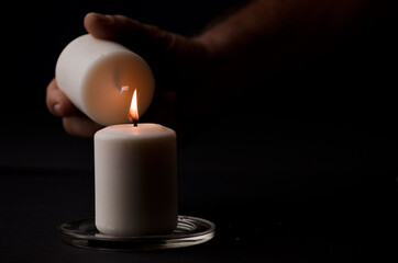 Obraz na płótnie Canvas burning candle with flame, man's hands lighting candle, black background. (focus on candle)