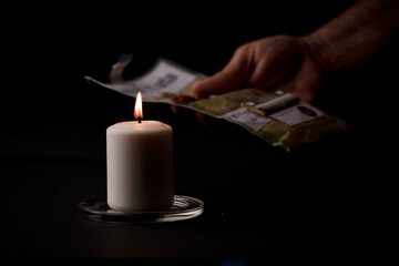 candle lit with flame, man's hands holding a cigar, black background. (focus on candle).