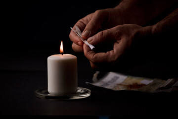 candle lit with flame, man's hands holding a cigar, black background. (focus on candle).