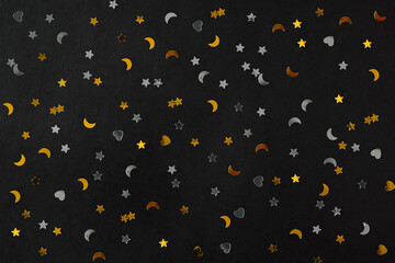 Silver and golden stars, hearts and moons on black decorating paper background. Backdrop for postcards or banners. Luxury new year 2022 decoration packaging. Merry xmas or birthday concept