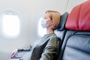 Young woman wearing face mask is sleeping on airplane. New normal travel after covid-19 pandemic concept