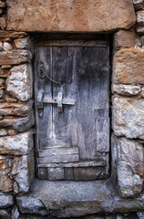 an old, rustic and deteriorated wooden door framed in a blue-gray tone on a stone wall in warm tones, vertical