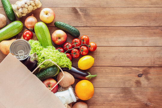 Paper grocery bag with fresh vegetables, fruits, milk and canned goods on wooden backdrop. Food delivery, shopping, donation concept. Healthy food background. Flat lay, copy space.
