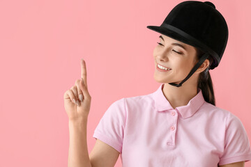 Beautiful female jockey showing something on color background