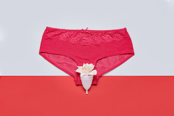 Menstrual cup with flower and female panties on color background