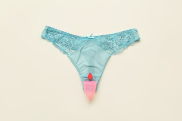 Menstrual cup and female panties on light background