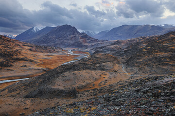 Mountain landscape on the background of a river and a stormy sky at sunset in autumn. Altai, Russia