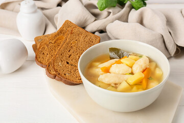 Bowl of tasty dumpling soup and slices of bread on light wooden background