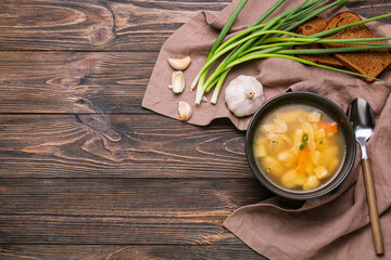 Bowl of tasty dumpling soup, green onion, garlic and bread on wooden background