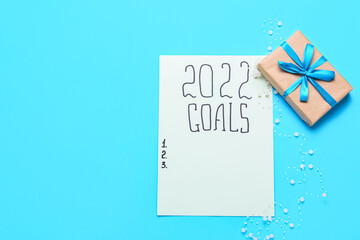 Paper sheet with text 2022 GOALS and gift on color background