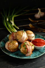 Plate of tasty baked potatoes with bacon and tomato sauce on dark wooden background