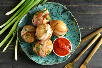 Plate of tasty baked potatoes with bacon, green onion and tomato sauce on dark wooden background