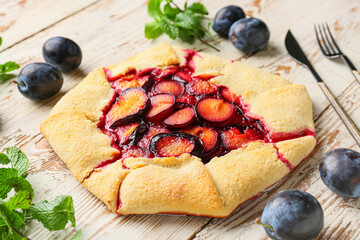 Tasty plum galette and mint on light wooden background, closeup