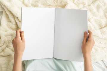 Young woman holding blank magazine on light background