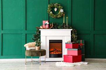 Modern fireplace with gift boxes and Christmas decorations near green wall