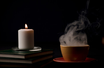burning candle with flame and cup of coffee with hot smoke. on the desk at home, power outage (focus on candle).