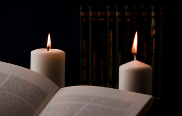 candles with flame, and reading book on desk, black background. (focus on candle).