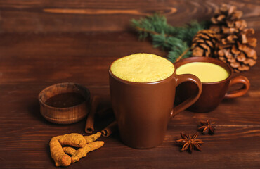 Cups of tasty turmeric latte with spices on wooden background