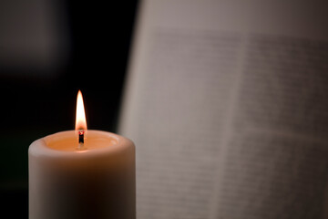 candles with flame, and reading book on desk, black background. (focus on candle).