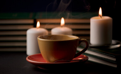 Obraz na płótnie Canvas cup of tea with hot smoke and three burning candles. on the desk at home, power outage (focus on cup).