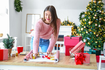 Beautiful young woman wrapping Christmas gift at home