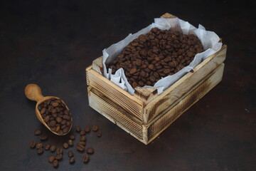 Closeup of roasted coffee beans in a small wooden crate, isolated on dark background. With wooden spoon.	
