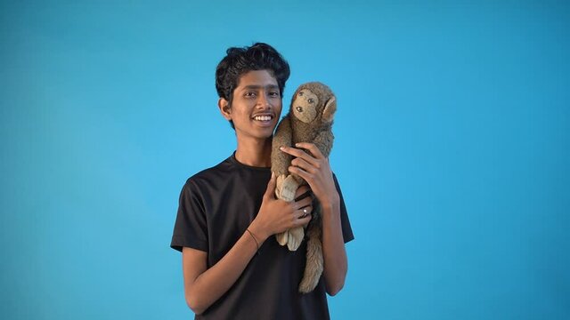 Smiling young Indian Puppet teenager relaxing with his puppet monkey in Blue Color Background Studio. Concept Of People Lifestyle