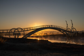 Fototapeta na wymiar Bicycle-shaped bridge with water fog rising from the beach