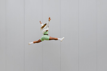 Young african american adult woman jumping with legs open and arms up in the air. Copy space. - Powered by Adobe