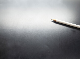 Fototapeta premium A white pencil on a white-gray-black area with a bright light.
