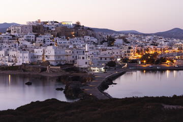 Obraz premium Pink morning over a mountainous Greek island with a white city. Street lights are reflected in the calm sea