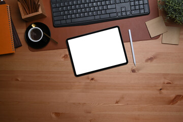 Digital tablet with white screen, stylus pen and coffee cup on wooden table.