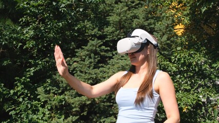 Female in virtual reality glasses controls the device with his hand against the background of green trees. getting experience using VR-headset glasses of virtual reality
