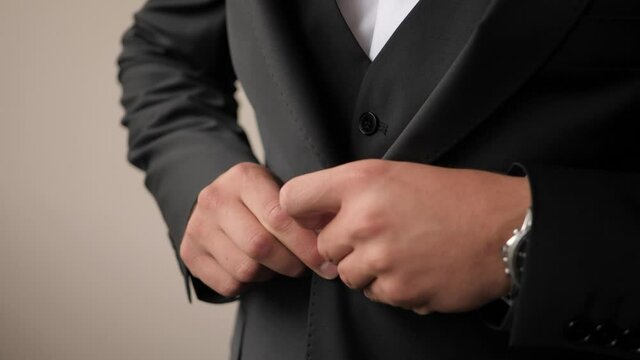Close-up shot of a groom getting ready and buttoning his black wedding suit wearing wooden bow tie and elegant watches.