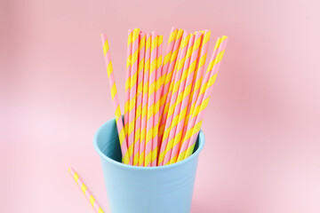 Stripped pink and yellow pastel color of  paper drinking straw in blue tin can of pink background - party, picnic, birthday and cute concept