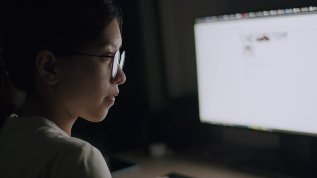 Asian female wearing glasses using computer searching data of online information for her work plan at night.