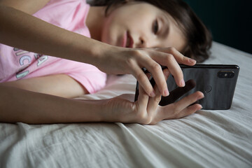 The child lies in bed and communicates with a friend in social networks on a smartphone. Gadget in...