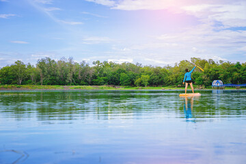 Obraz premium Young woman have fun on stand up paddleboard. Active paddle boarder paddling at the lake. Water sport, SUP surfing tour in summer holiday vacation.