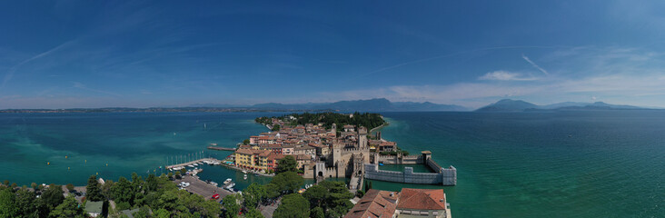 Aerial panorama of Sirmione castle, Lake Garda, Italy. Top view of the 13th century castle. Italian castles Scaligero on the water. Flag of Italy on the towers of the castle on Lake Garda.