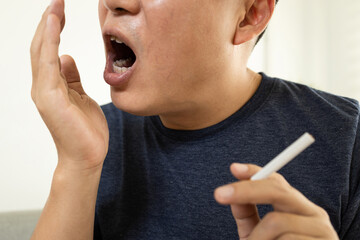 Man holding a cigarette,checking his breath with hand has bad breath,oral odor from tobacco...