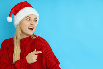 Attractive girl in Santa hat on blue background, space for text