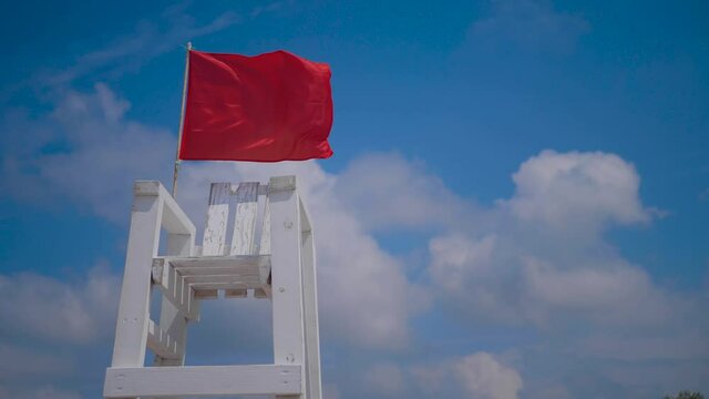 empty white wooden rescue chair on the beach with a red flag waving