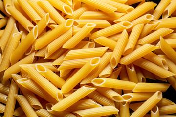 Raw penne rigate pasta close up on black background.
