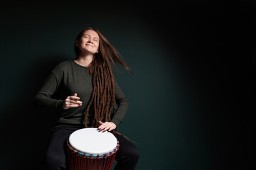Percussion musician. Pretty young woman playing djembe. Green background.