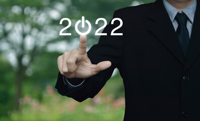 Businessman pressing 2022 start up business flat icon over blur flower and tree in park, Business happy new year 2022 cover concept