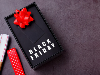 Top view, the word "Black Friday" on black gift box with red bow and white and red ribbon on dark grey background. Flat lay, copy space.
